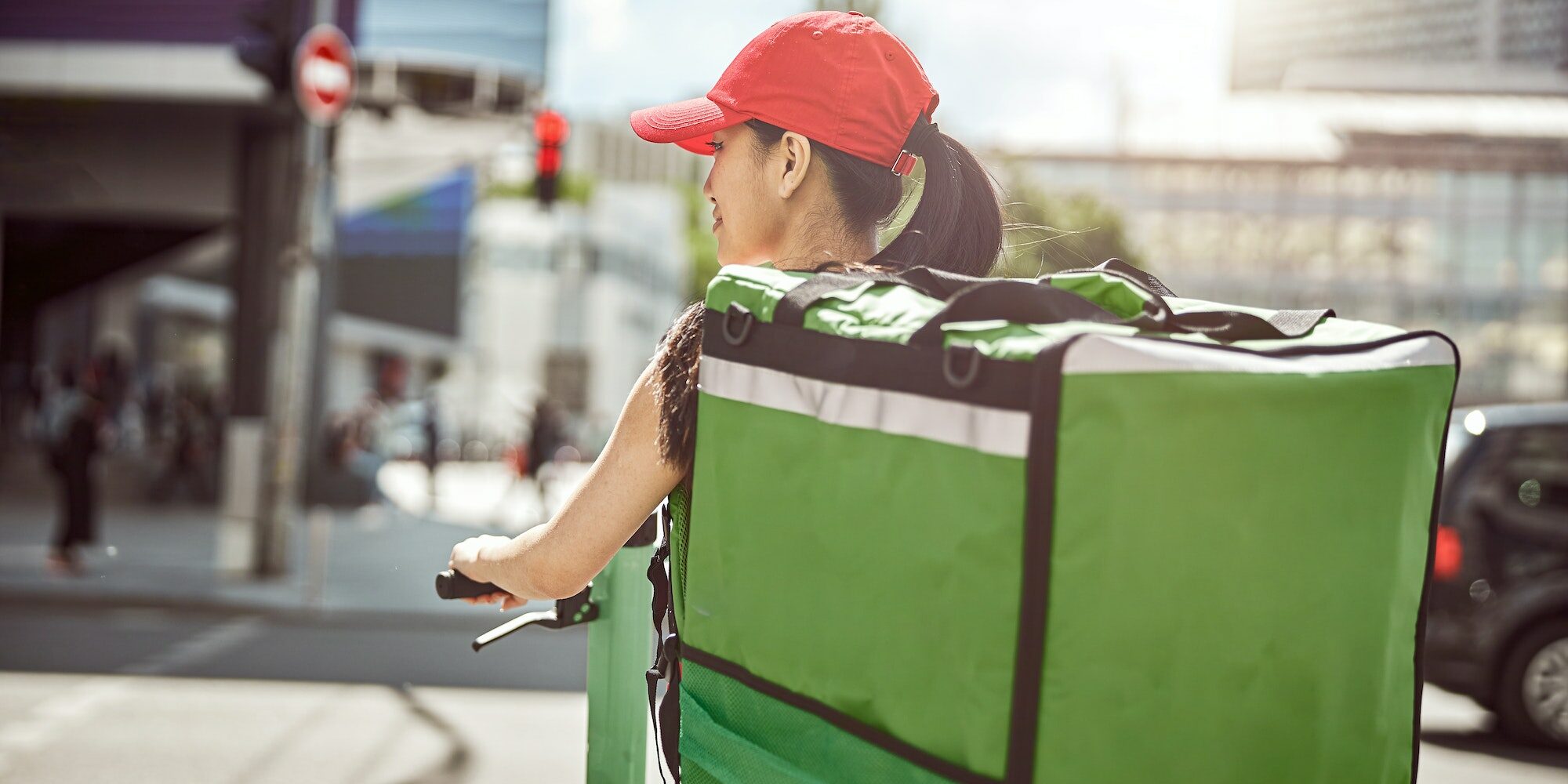 Food courier on scooter carrying food delivery bag through city